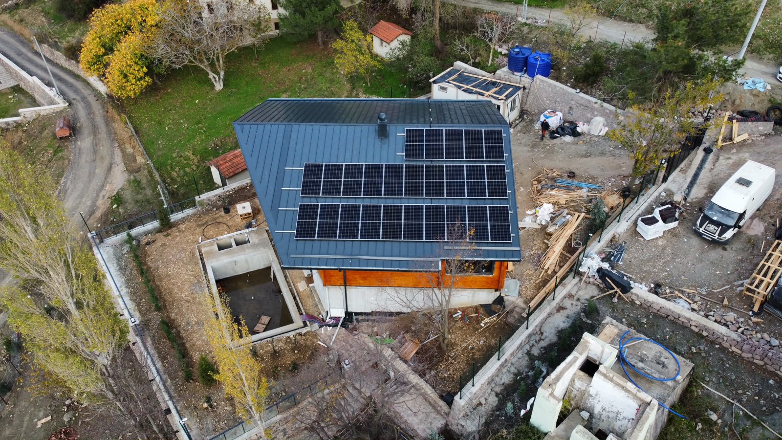 Ahşap cepheli evin metal çatısındaki güneş panelleri, havadan görünüm