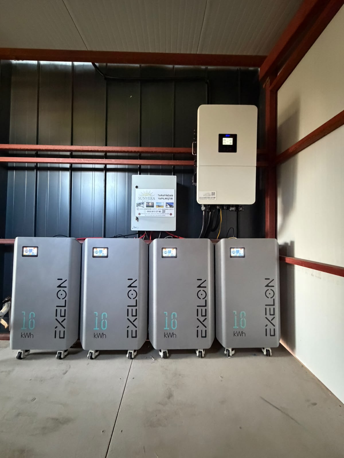 Duvardaki inverter ve altında yan yana dört batarya modülü